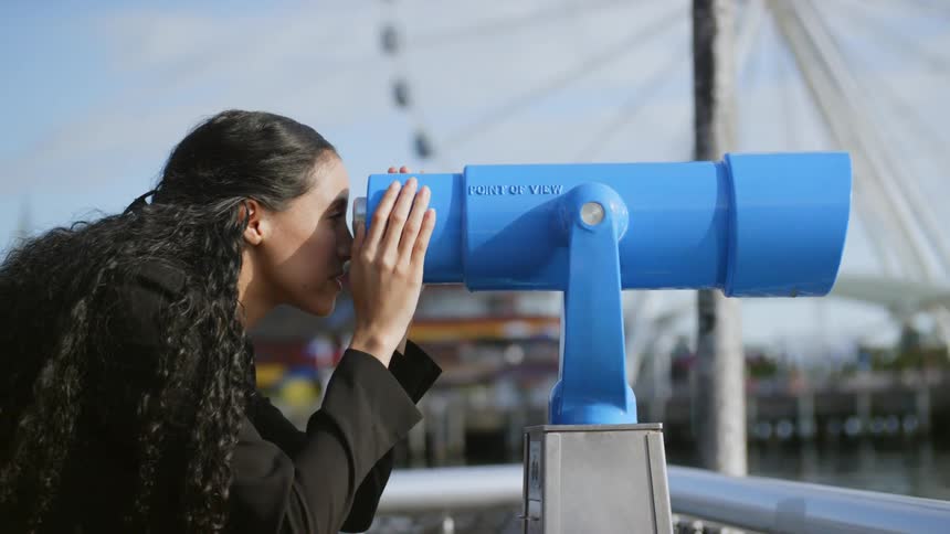 A woman is looking out of a telescope on the pier