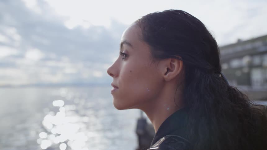 A woman stands on a pier and looks out at the ocean sparkling in the sunlight