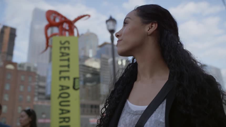 A woman walks past a group of people and a yellow seattle aquarium sign