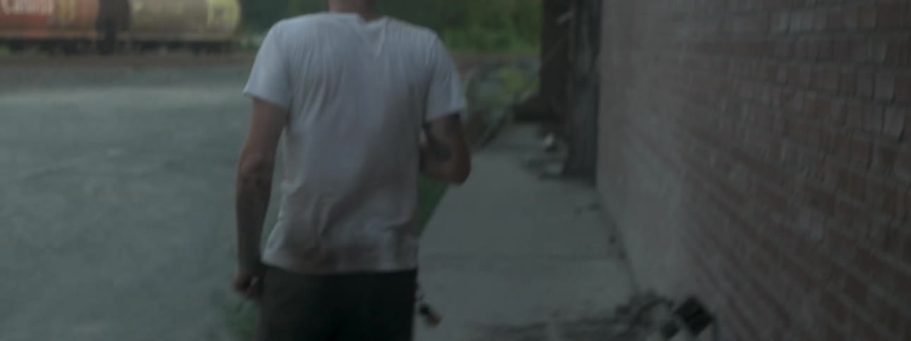 A man in a white shirt walks behind a building