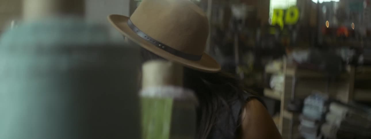 A woman in a light brown hat is chewing gum and looking through fabric