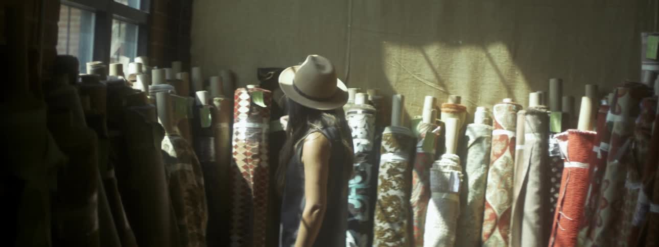 A woman in a straw hat looking at rolled rugs