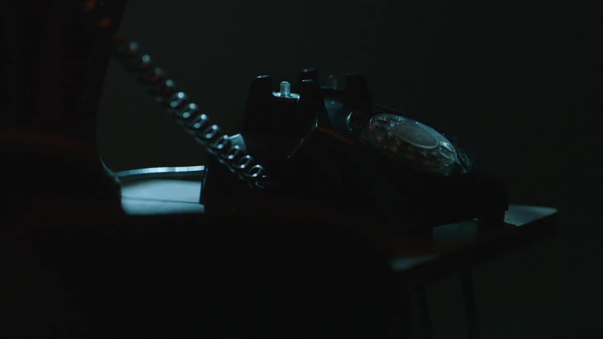 A person answers a black phone in a dark room, then hangs up