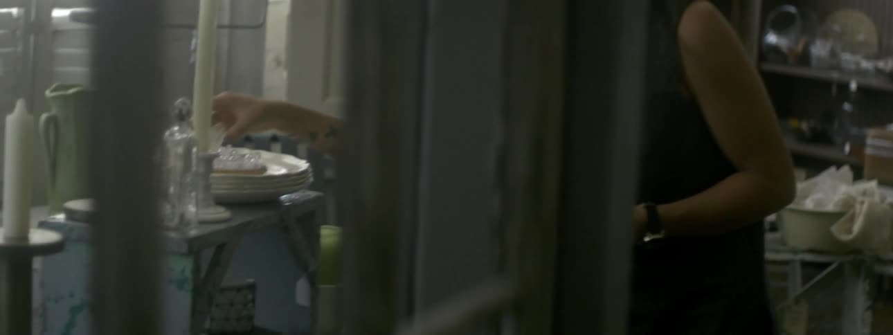 A woman wearing a hat looks around and picks up interesting items in a thrift shop