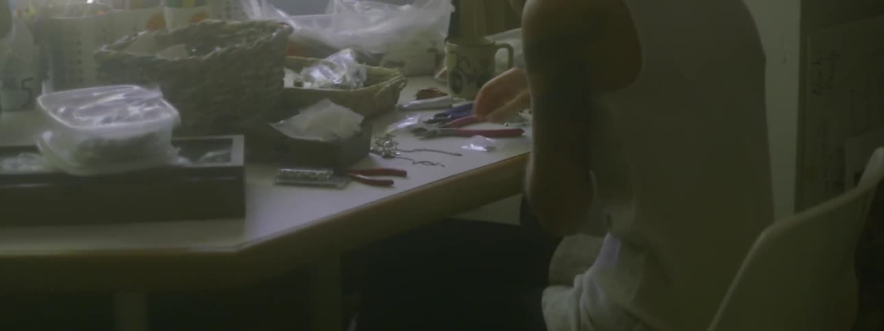 A woman sitting at a table is making jewelry