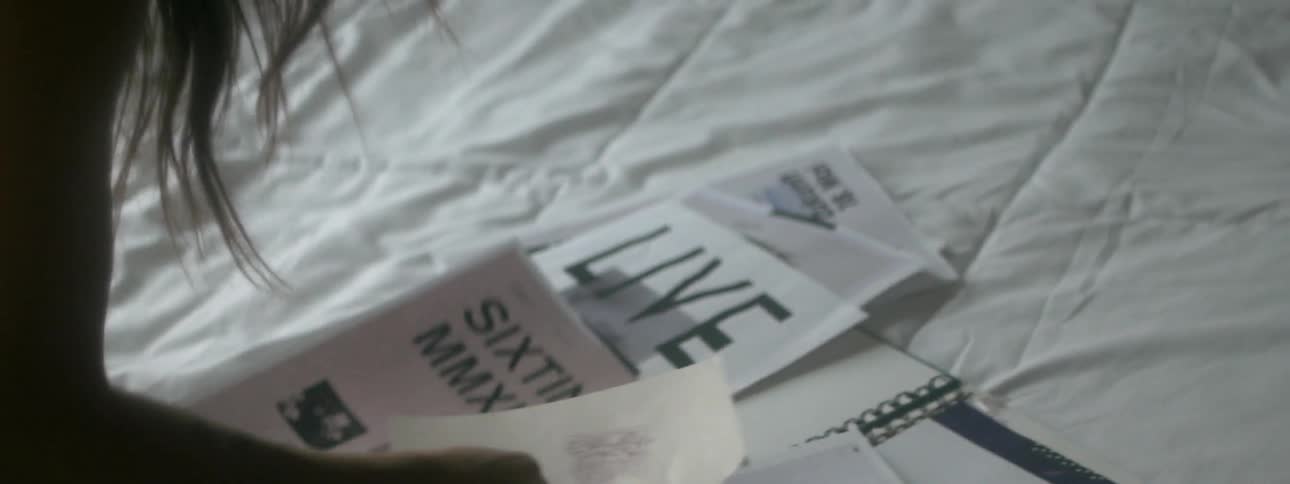 A woman sorting through sketches and flyers laid out on a bed
