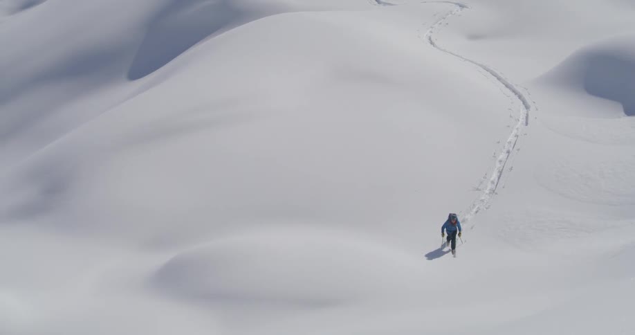 A man with green jacket walks in the snowy mountain