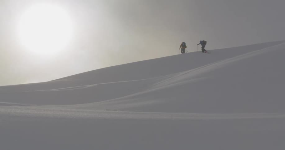 Two people climb over the snowy hill