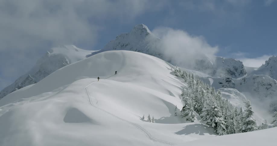 Two people climb a steep snow covered mountain