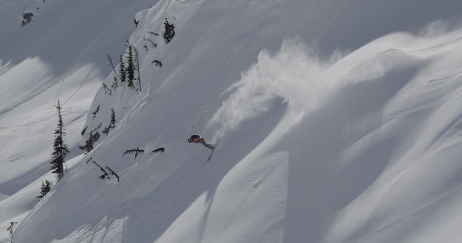 Skier jumps and flips in air then falls on steep snowy slope