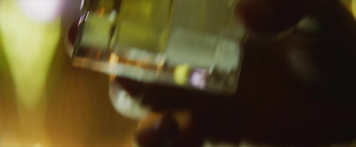 A glass half full of a yellow liquid with ice is raised