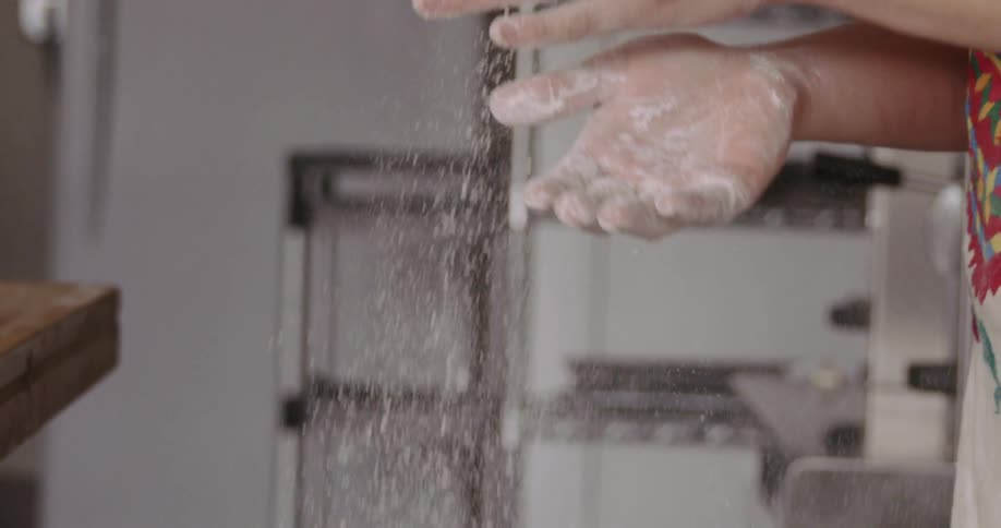 A person claps their hands together while they are coated in flour as they stand in a large kitchen area