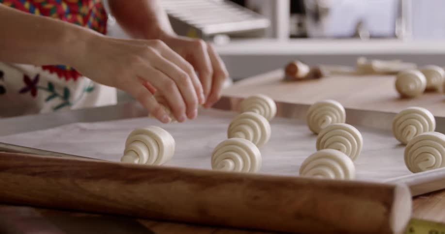 Woman places roll shaped raw dough on baking sheet