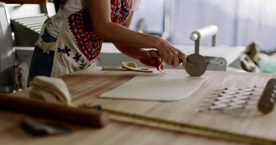 A woman uses a pastry wheel cutter to cut strips of dough