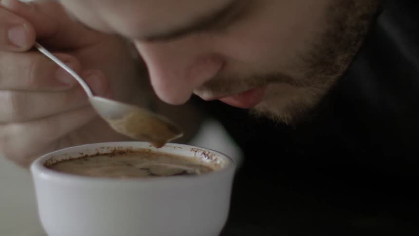 A man is smelling and stirring his coffee