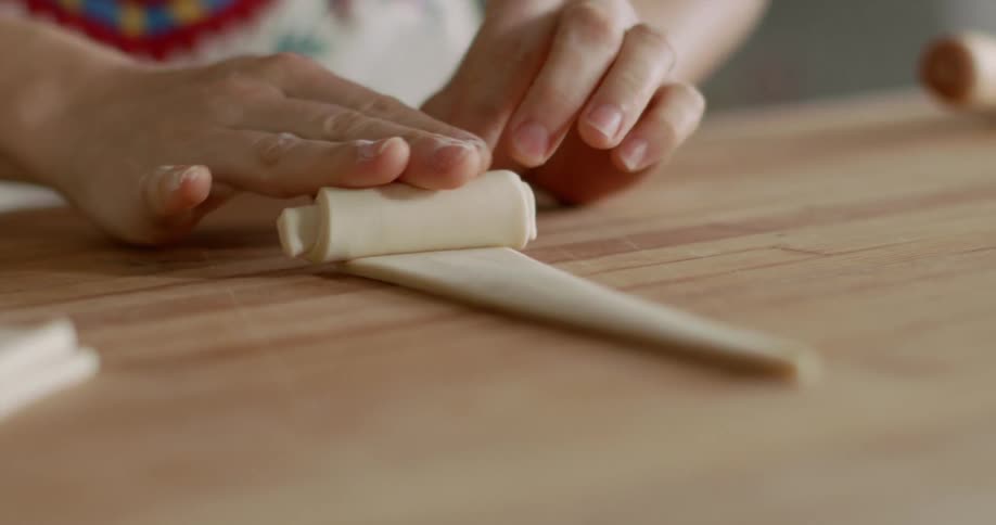 A woman is rolling a triangle shaped piece of dough on a wood counter