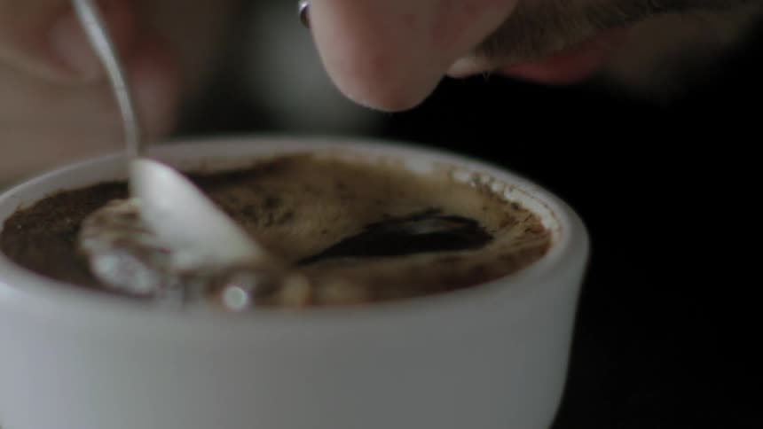 A person is stirring coffee with a spoon during cupping