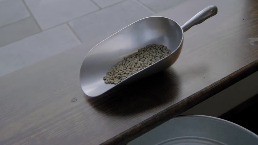 Metal scoop with beans sitting on a narrow wood table
