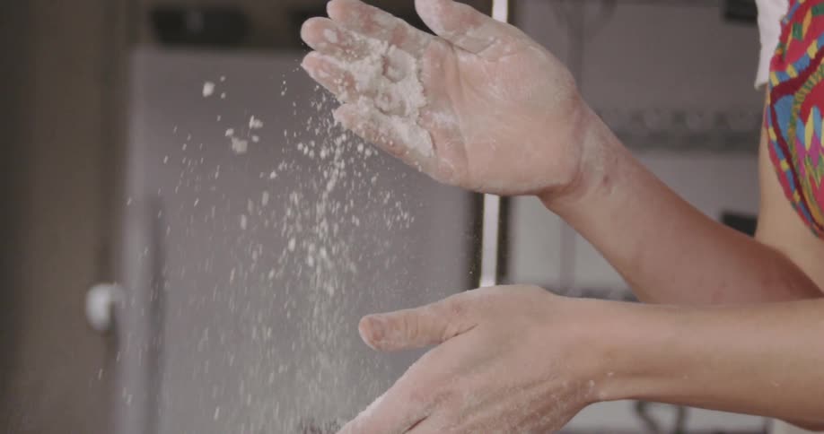 Flour flies through the air while a person claps their hands together while baking in a kitchen