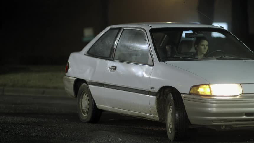 Woman sitting in a parked car with headlights on at night