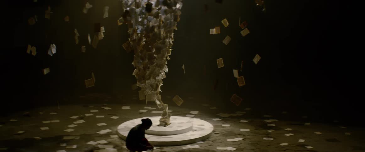 A woman bends down to pick up book pages from a floating art installation