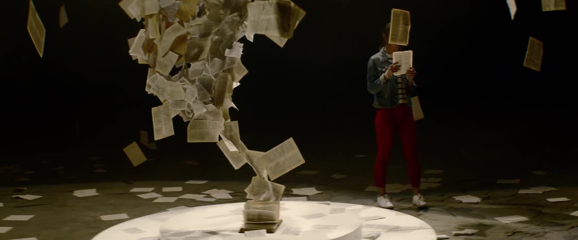 Woman walks around paper sculpture reading hanging sheets