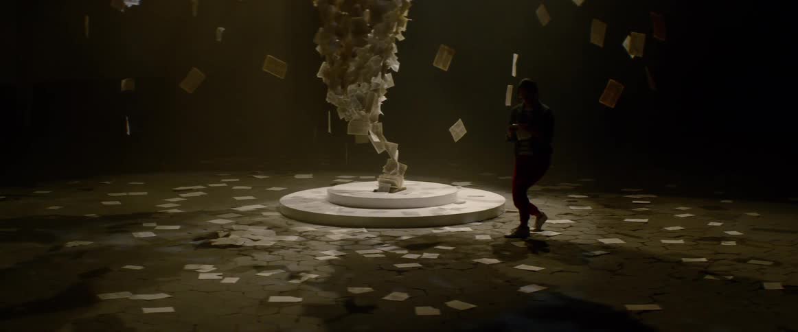 A woman kneels down and picks up a paper from the floor around a paper art sculpture
