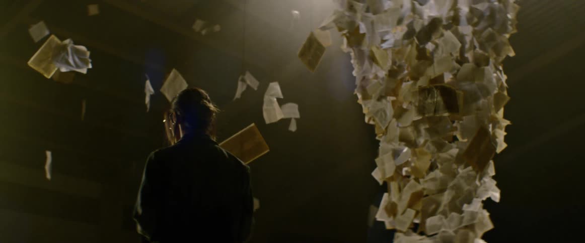 A woman reaches up and touches a piece of paper hanging by a wire in an art installation