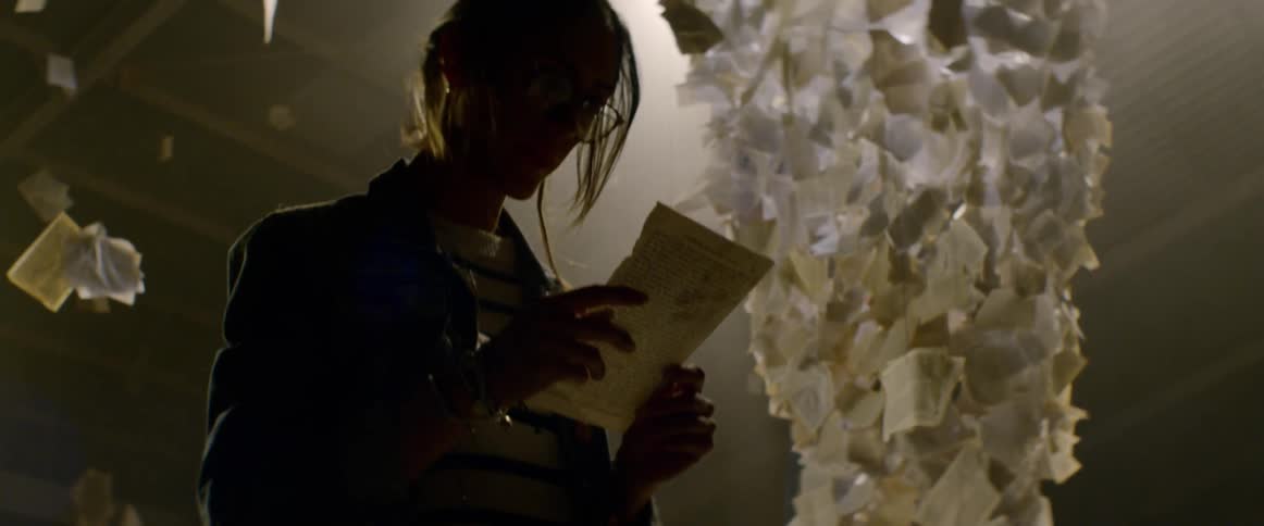 A woman reading at an art installation containing postcards and pages of text suspended from the ceiling