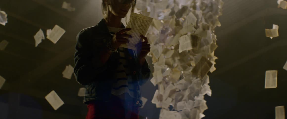 A female artist picks up a piece of paper and looks behind to the tall structure