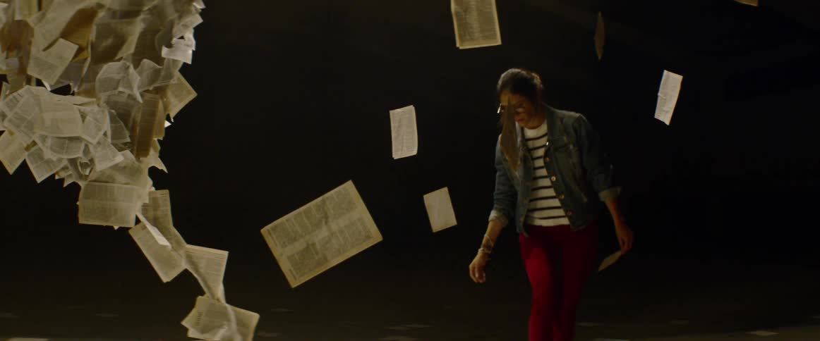 A woman picks up a piece of paper on the floor beside a tall paper art structure
