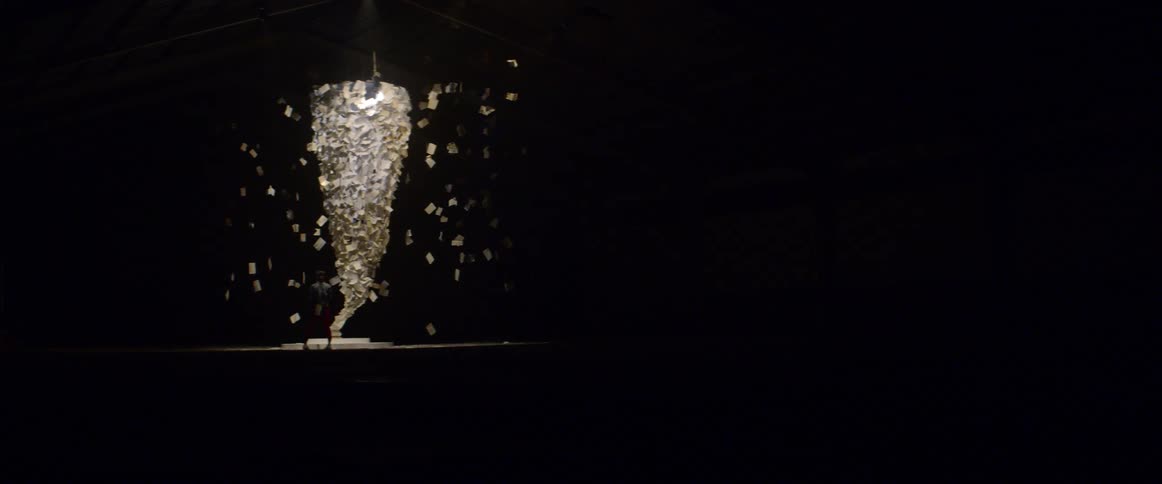 A woman looks at an art installation containing postcards and pages of text suspended from the ceiling