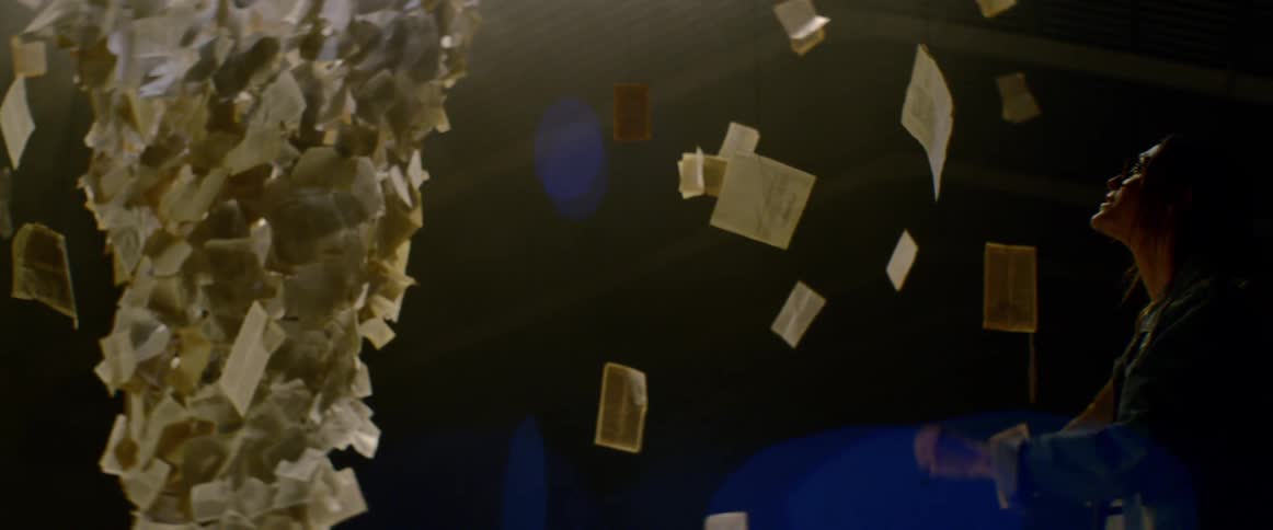 An art installation containing postcards and pages of text suspended from the ceiling as a woman examines them