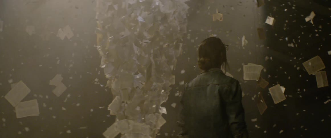 A woman walks around and art installation with confetti falling and paper hanging from wire