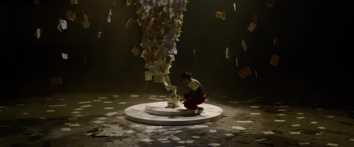 A woman kneels on the podium of a large paper art structure
