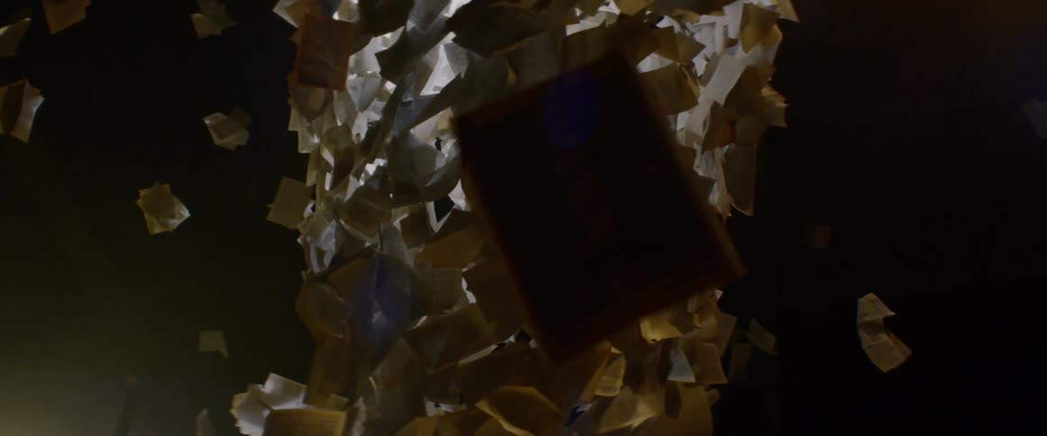 An art installation made of floating papers is shown in a dark room