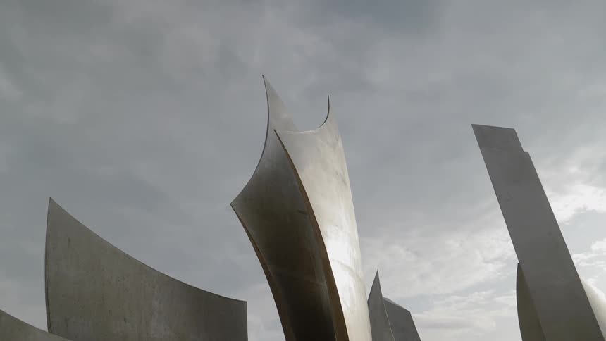 A monument made of curved pieces of steel stands tall under a cloudy sky