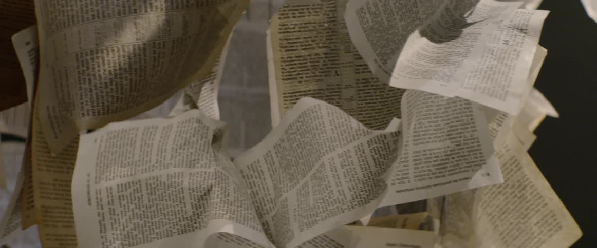 A woman walks around and looks up at pages hanging from the ceiling in an art installation