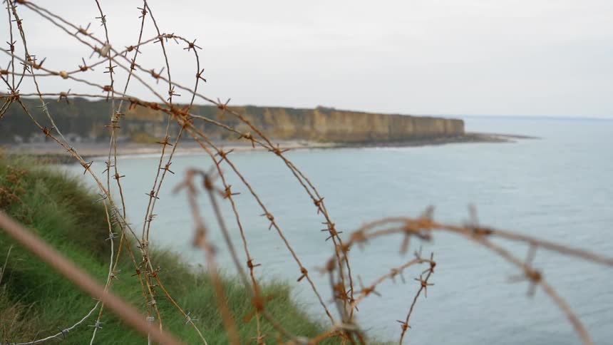 Barbed wire lines a grassy area above a beach