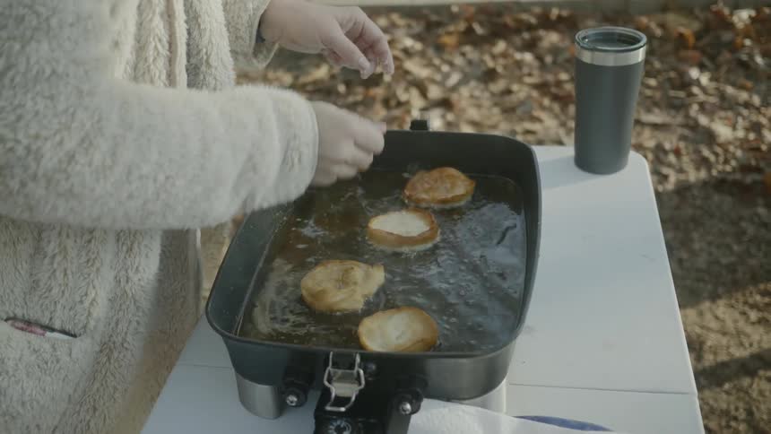 A woman deep fries donuts at a campsite
