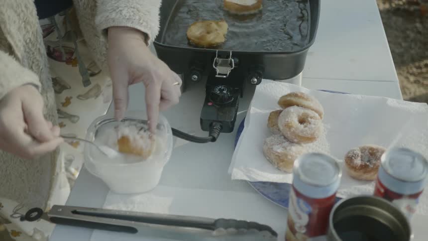 Woman prepares fried doughnuts covered in sugar outdoors