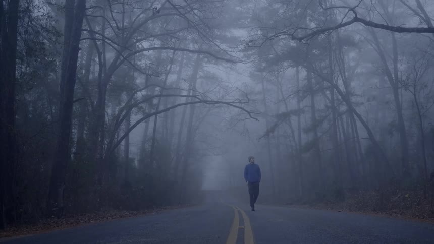 Man walks on the road in the foggy forest