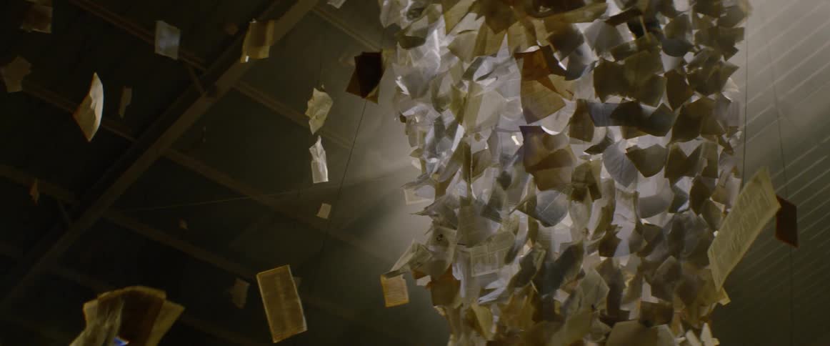 A paper and light art sculpture is surrounded by pages hanging on wire from the ceiling