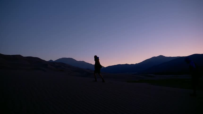 Two people walking in the evening are silhouetted against a dim sky
