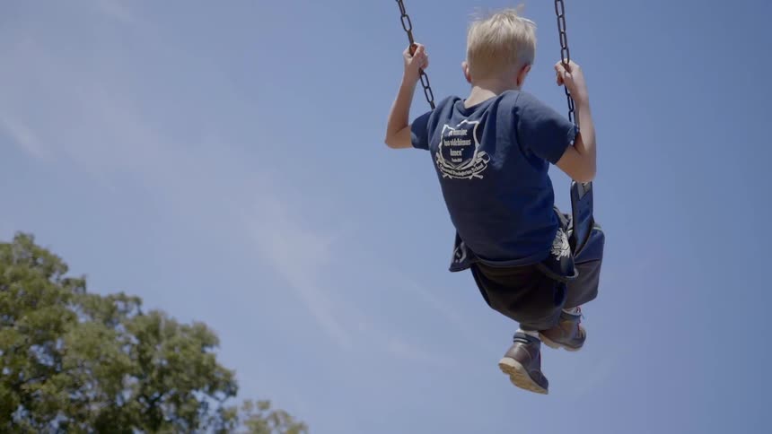 Boy swings high on playground swing under blue sky