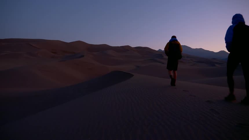 Two people walk down an empty road at night near the mountains