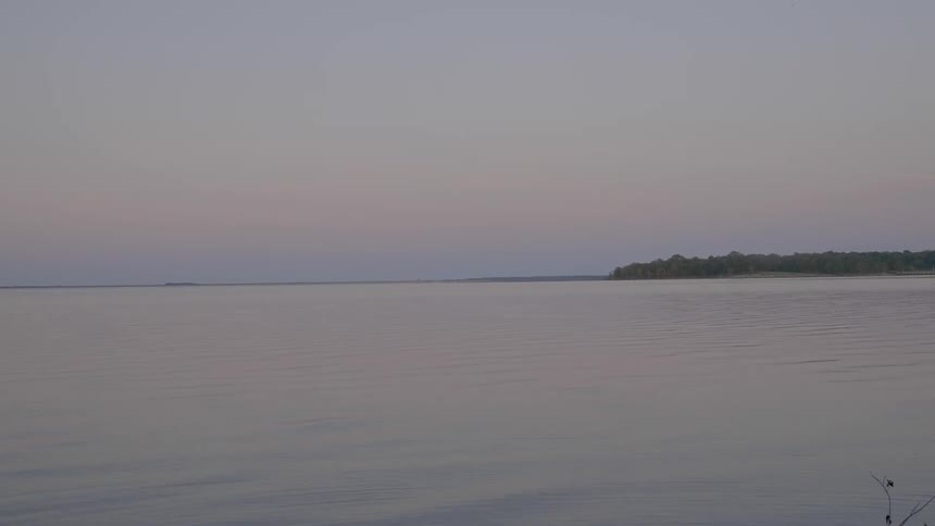 The water is calm near the shore at sunset
