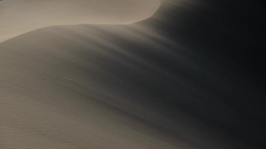 Wind kicks up a dust storm over a large desert sand dune