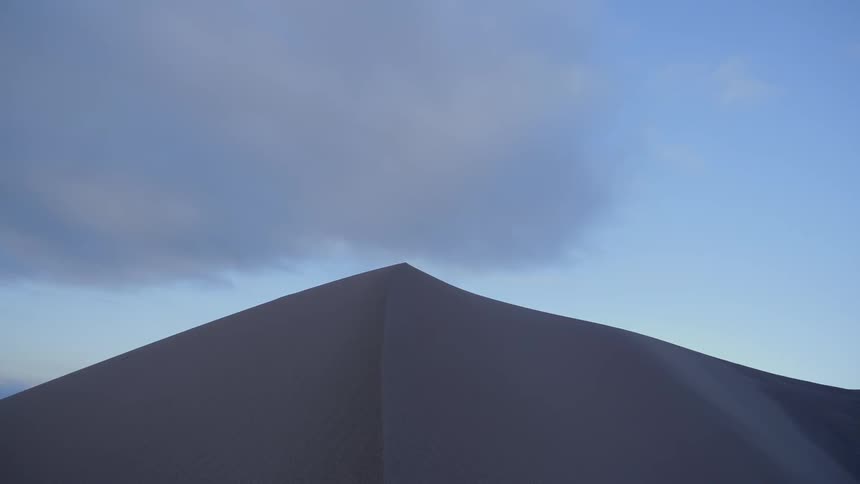 The peak of a sand dune is silhouetted against a blue sky