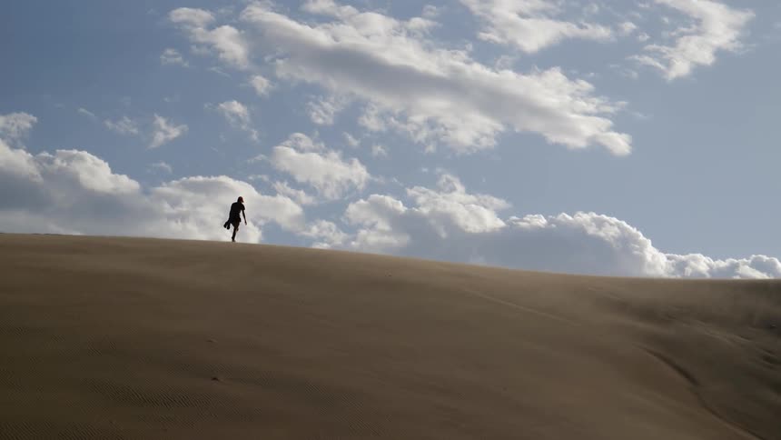 Womans silhouette walks uphill in the desert